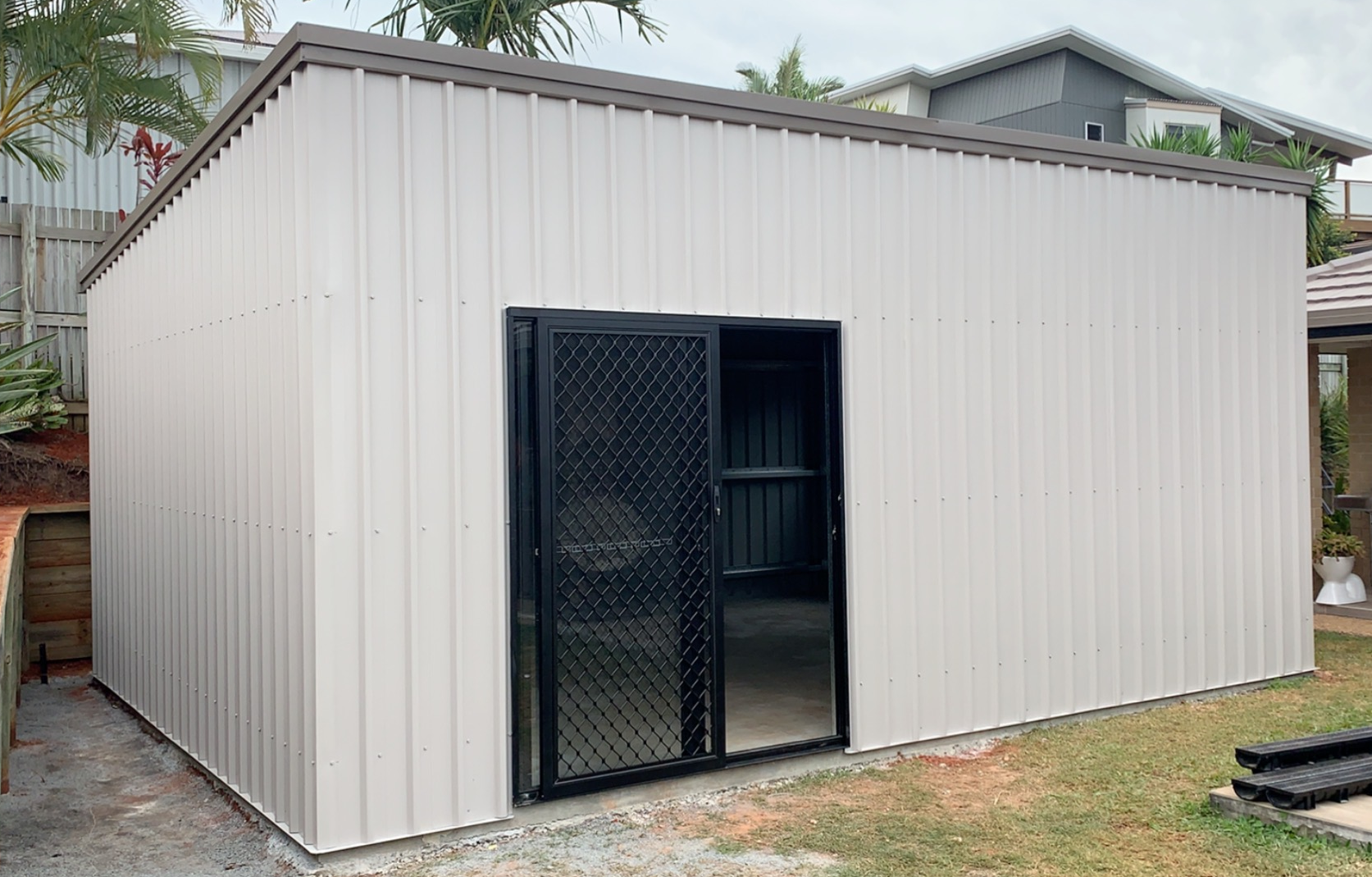 A white metal shed with a black door and fence in the backyard.