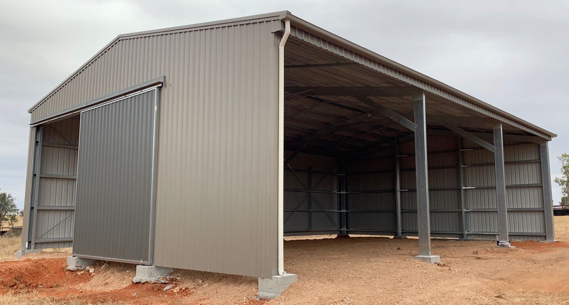 A large metal building with a sliding door is sitting on top of a dirt field.