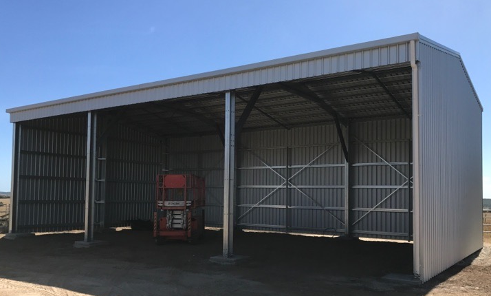 A truck is parked under a shed with a blue sky in the background