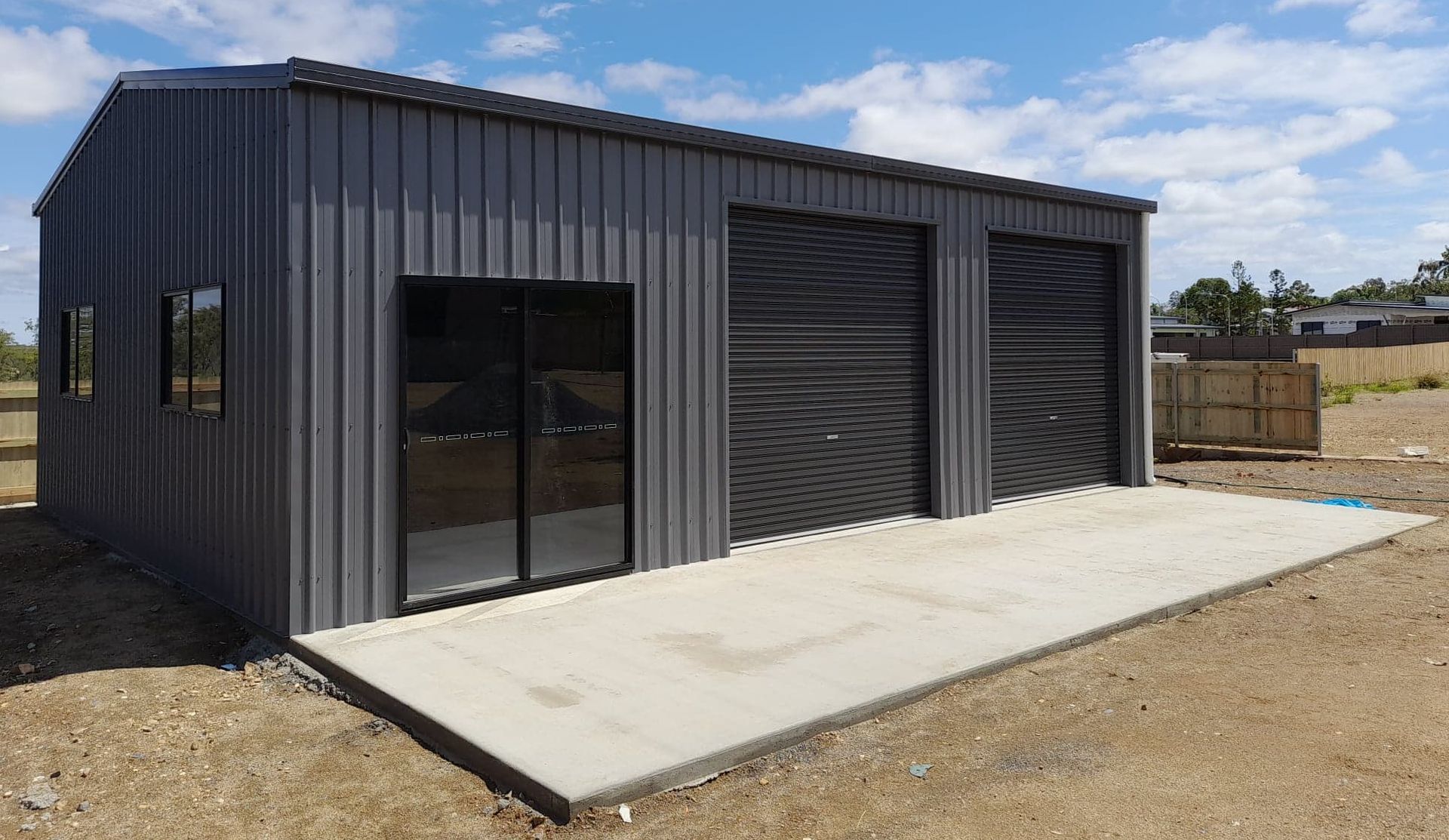 A gray metal building with three garage doors is sitting on top of a dirt field.