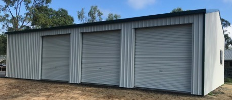 A garage with three roller doors is sitting in the middle of a field.