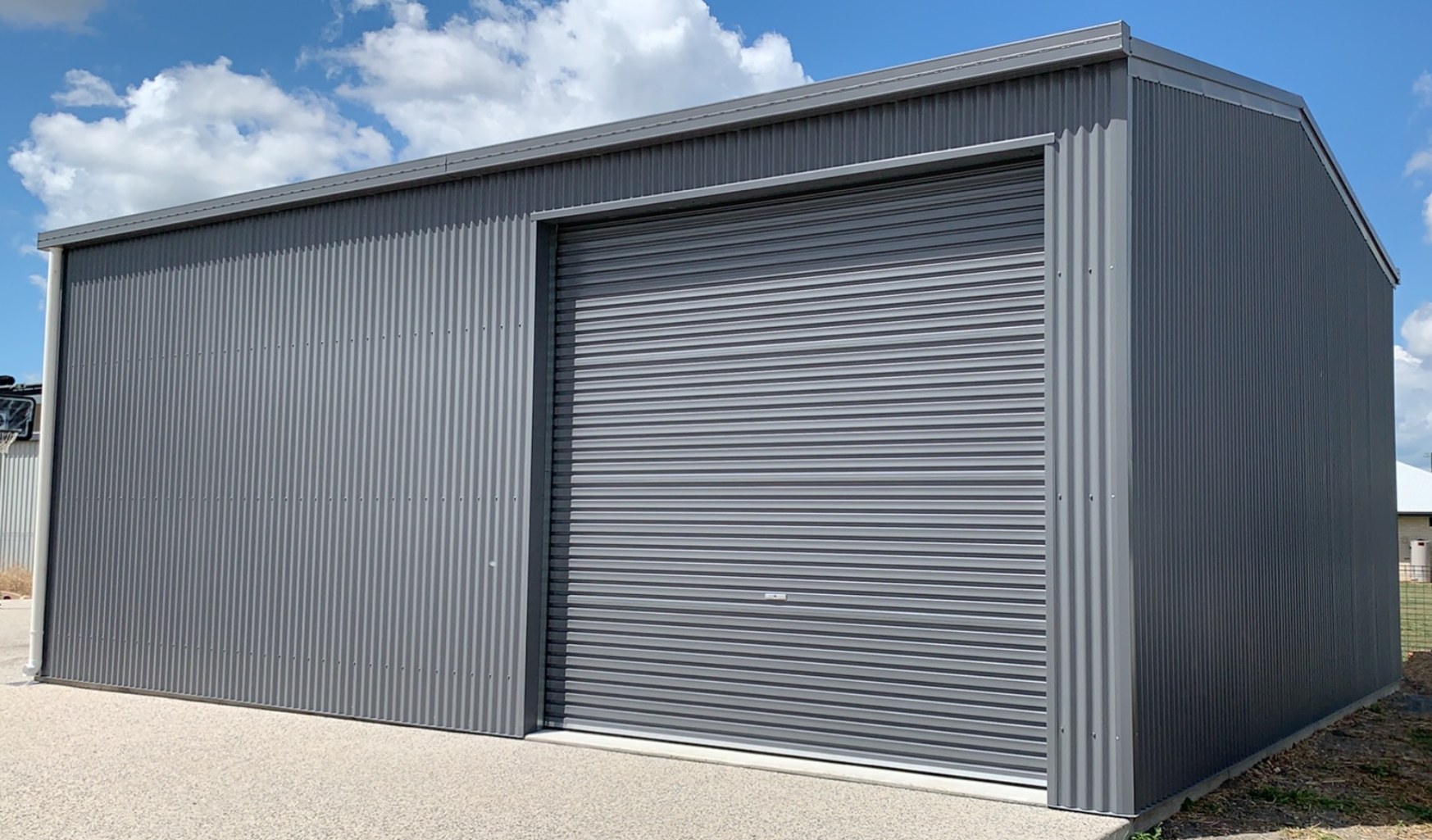 A gray garage with a roller door is sitting on top of a gravel driveway.