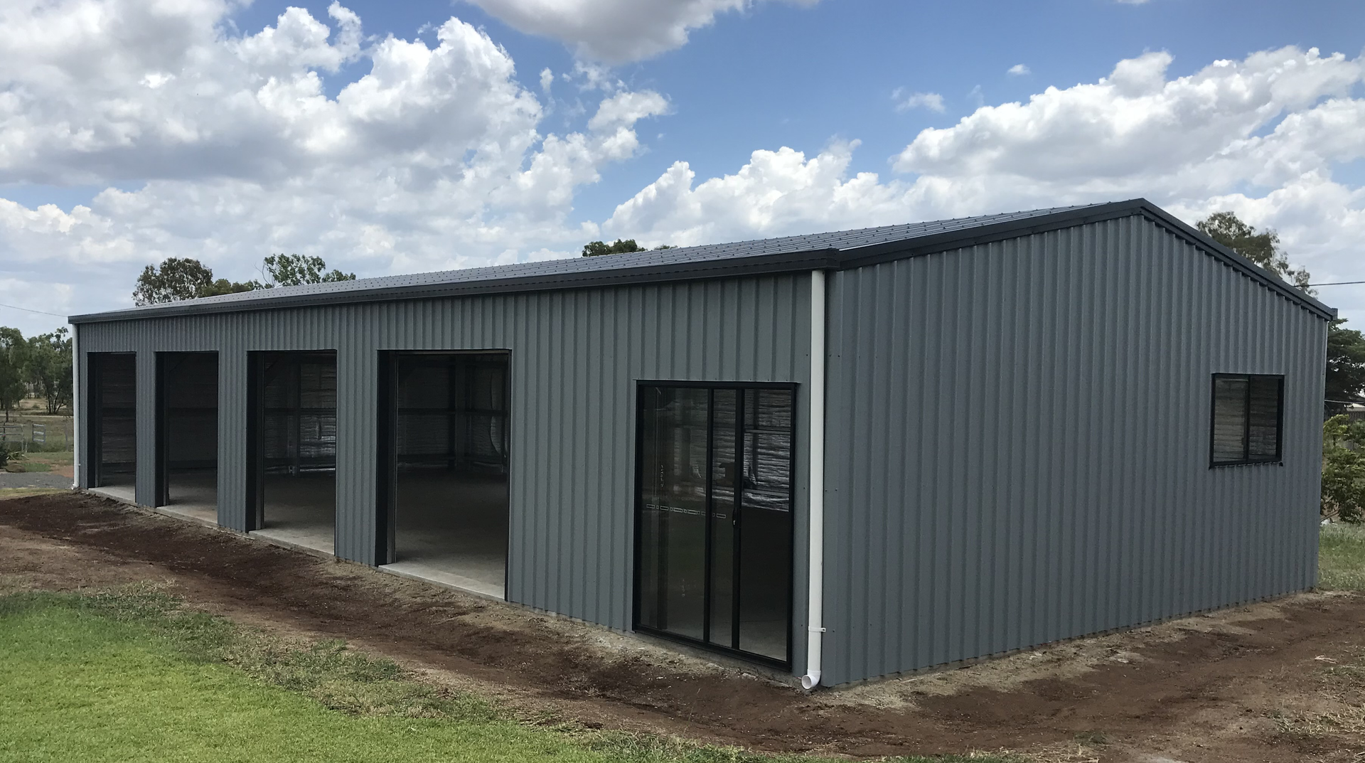 A large gray metal building is sitting in the middle of a grassy field.