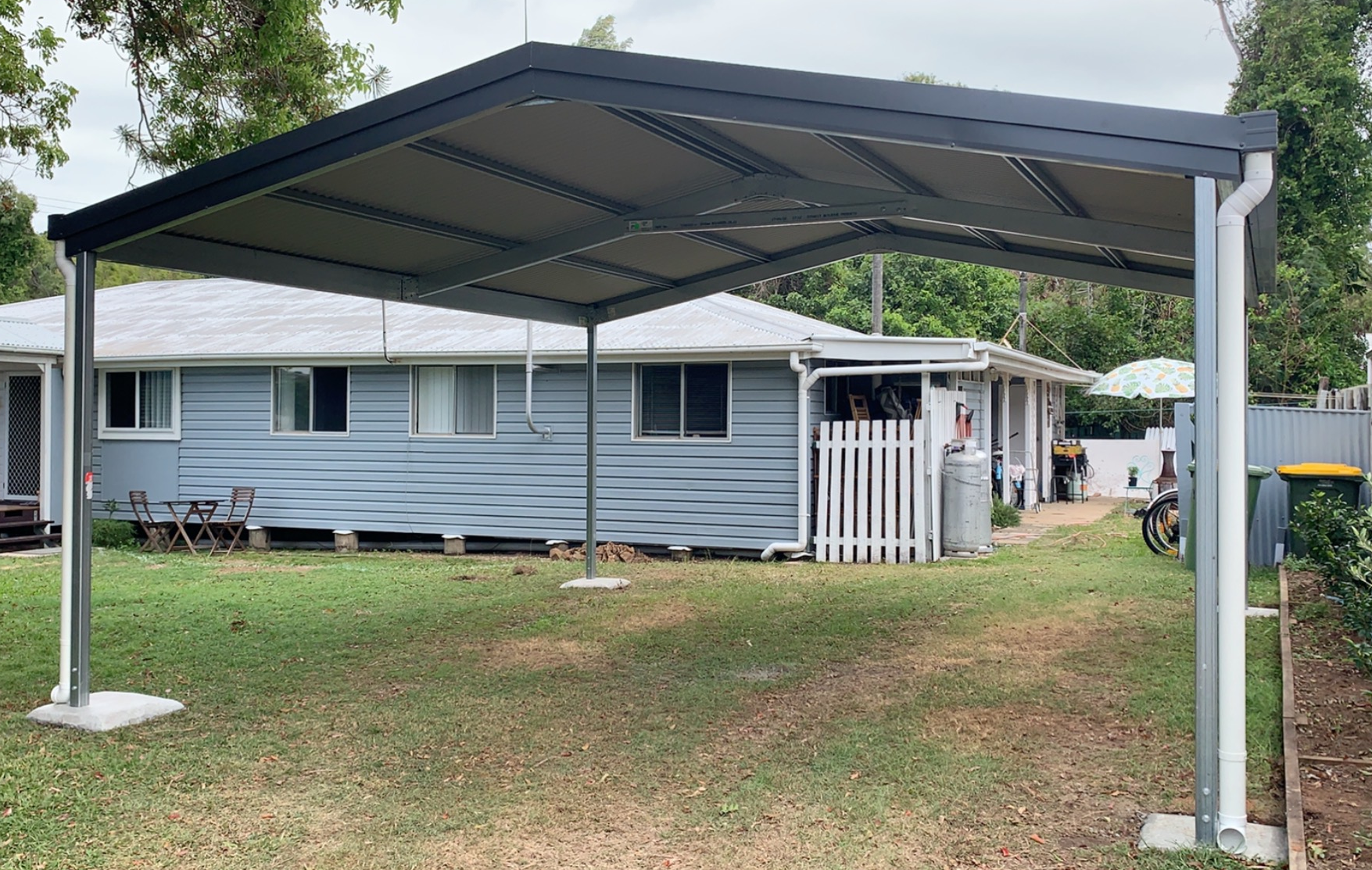 A carport is sitting in the grass in front of a house.
