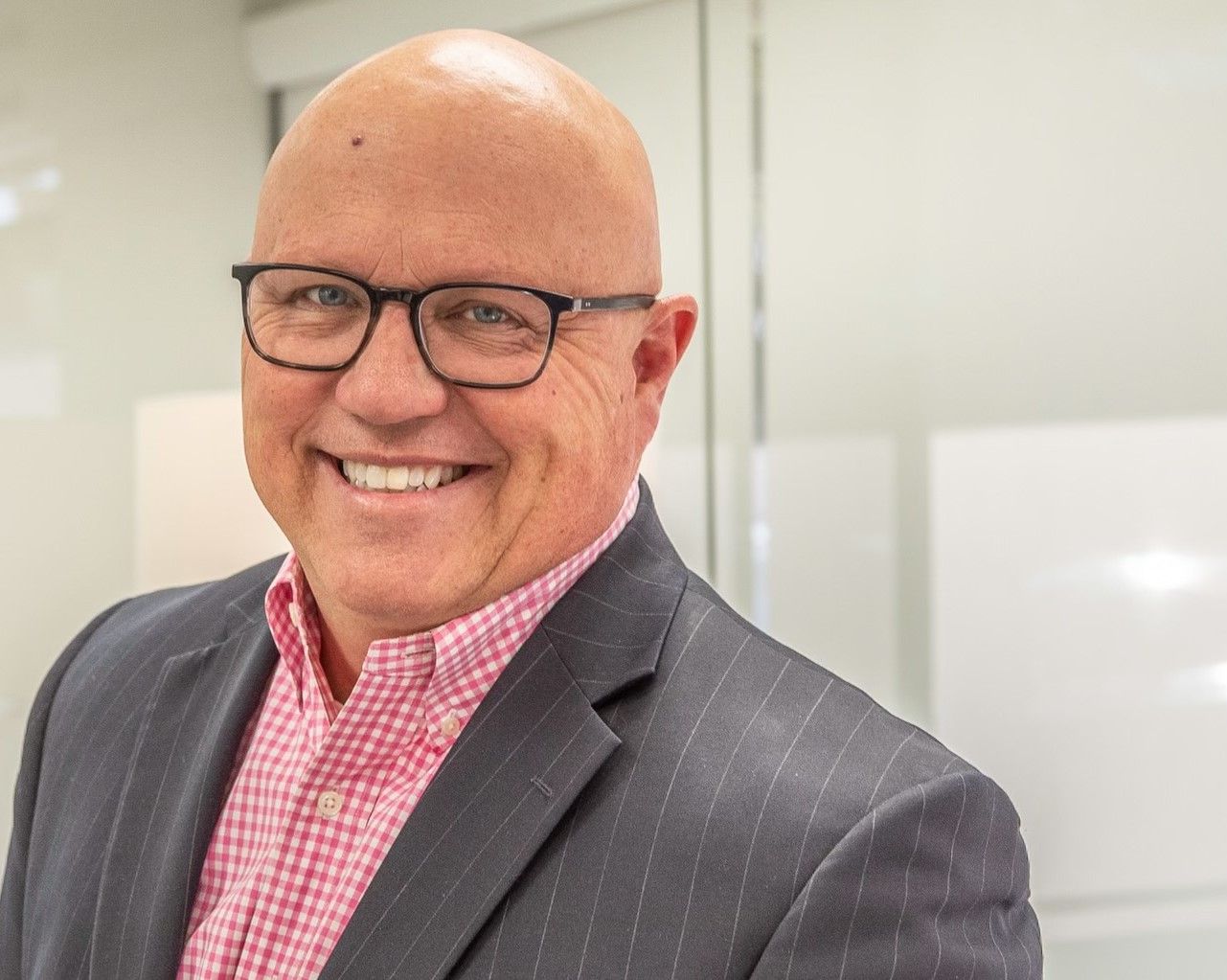 Man in glasses smiling, wearing a pink shirt and pinstripe blazer.