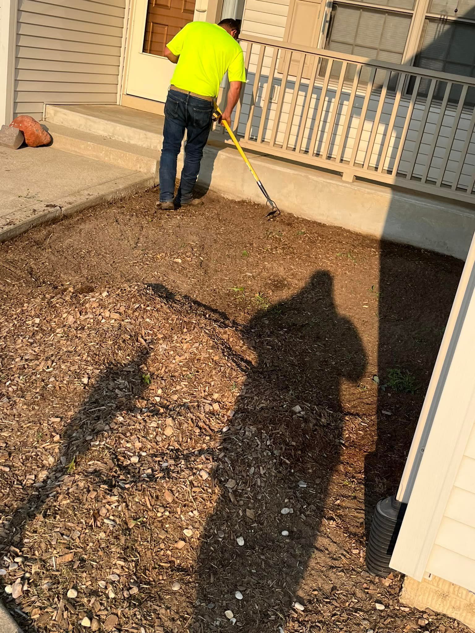 A man is raking gravel in front of a house.