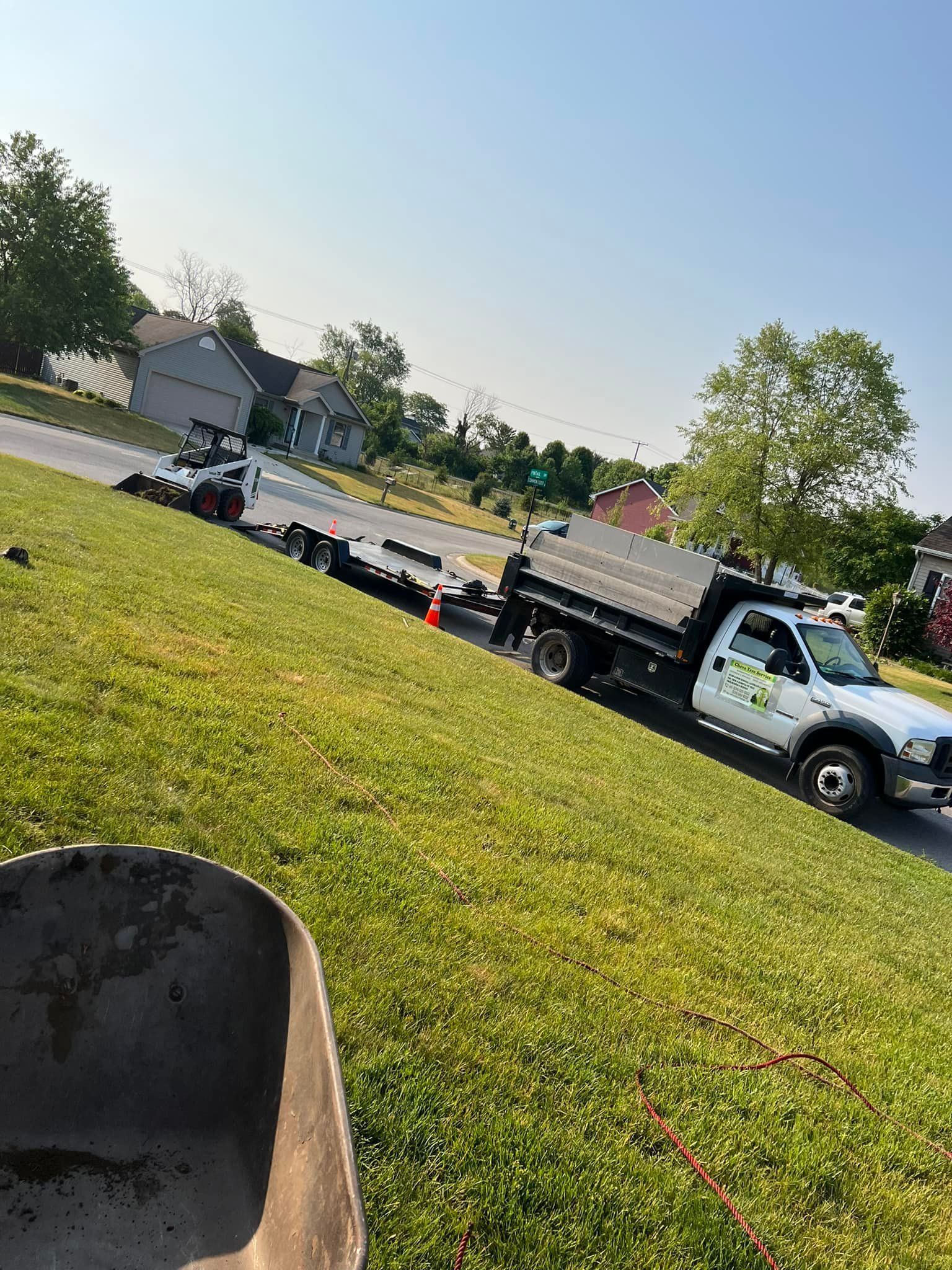 A white truck is parked on the side of the road next to a wheelbarrow.