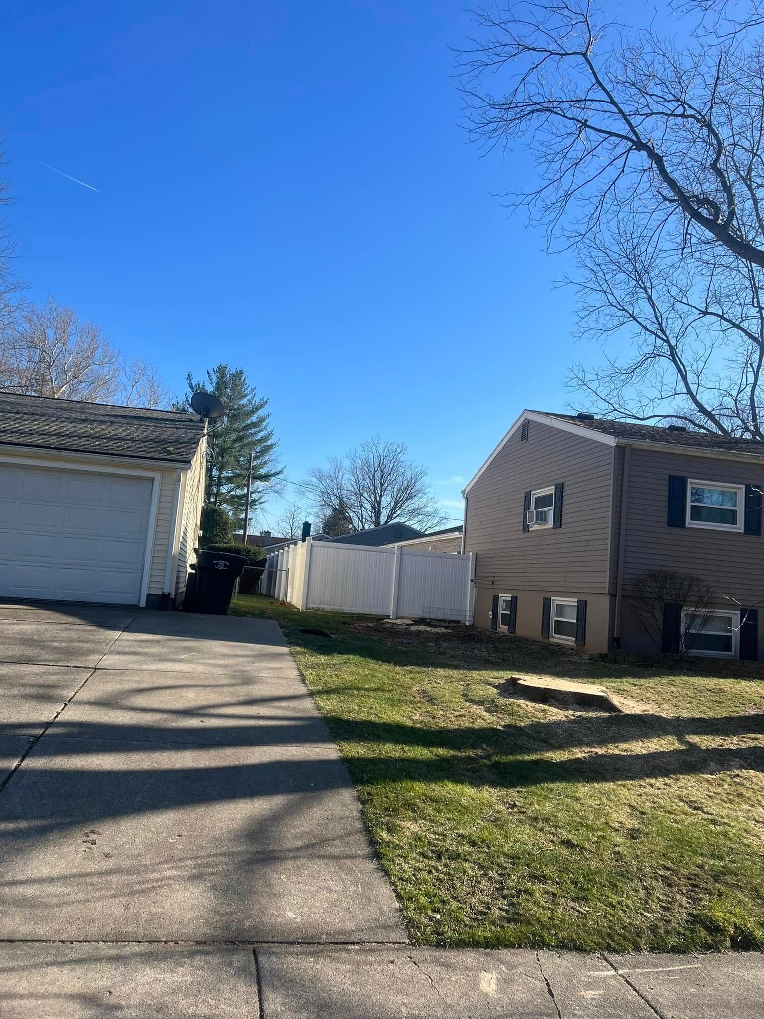 A driveway leading to a house with a garage and a white fence.
