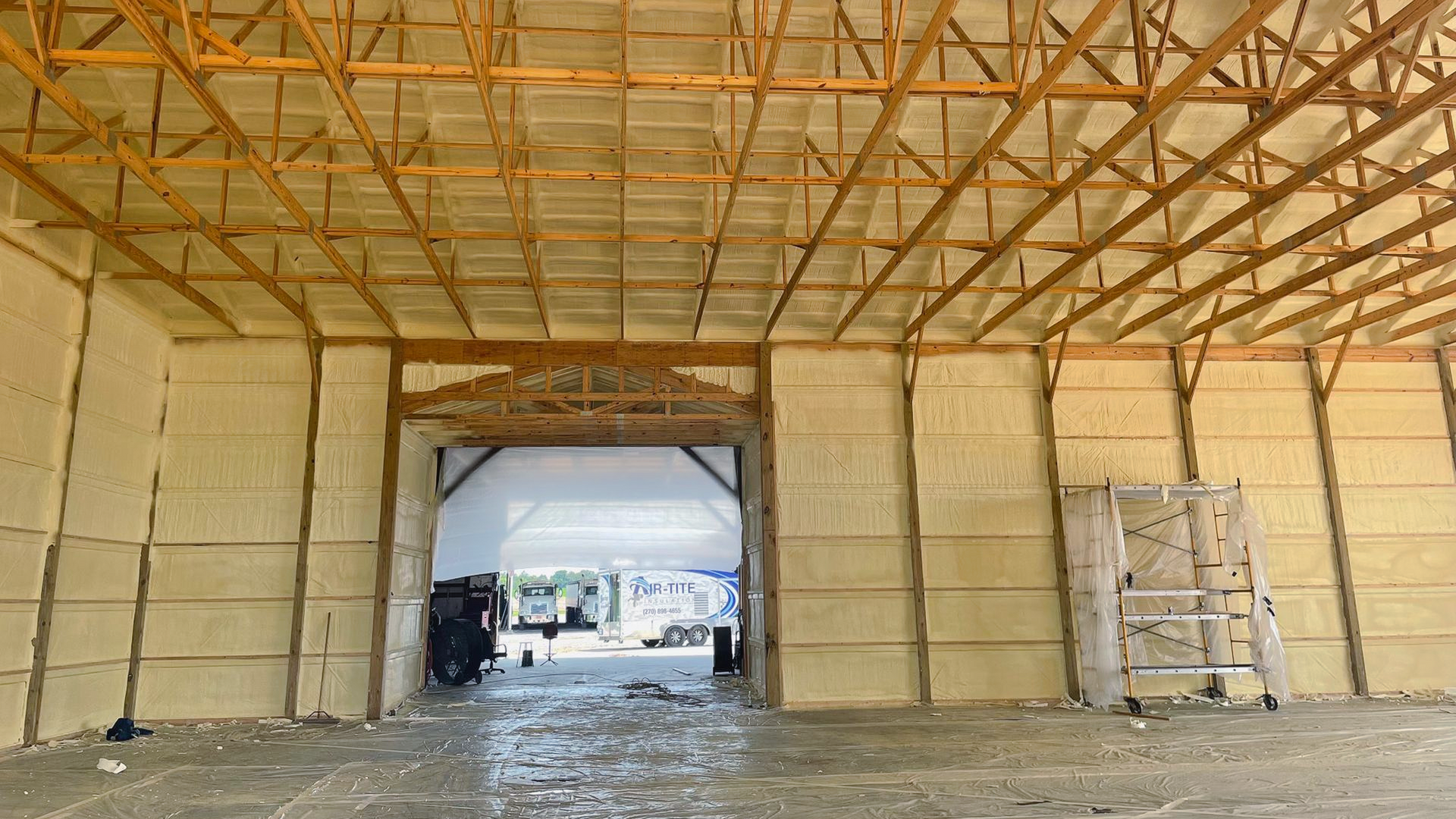 Interior of a barn with spray foam insulation on walls and ceiling. Open doorway reveals outdoor view.