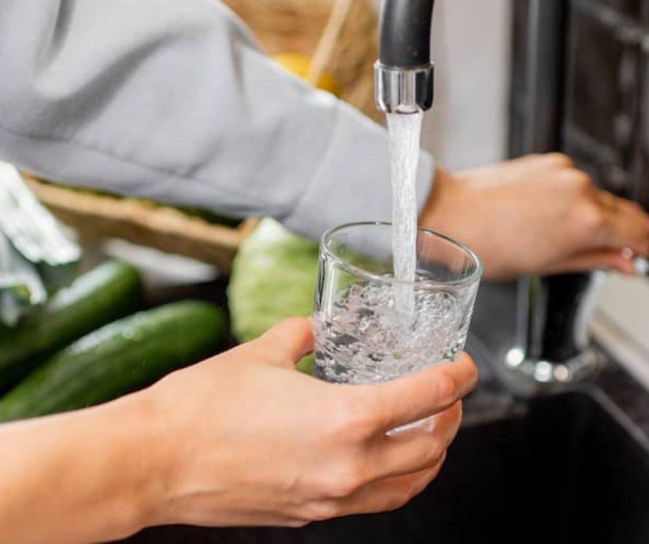 A person is pouring water into a glass from a faucet.