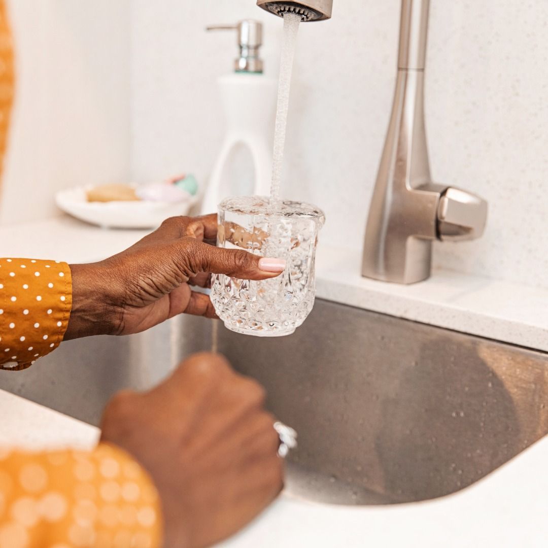 A person is pouring water into a glass in a sink.
