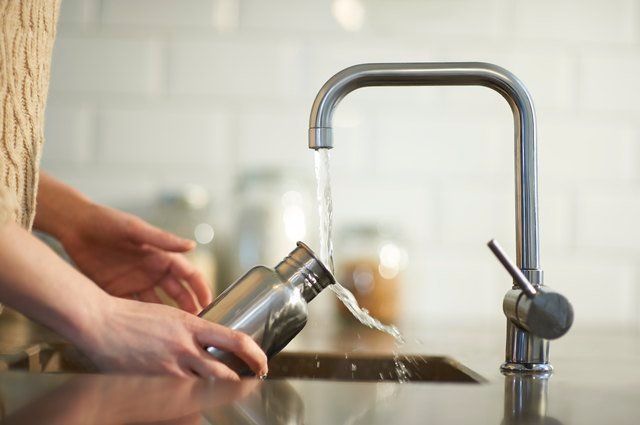 A person is washing a stainless steel water bottle in a kitchen sink.