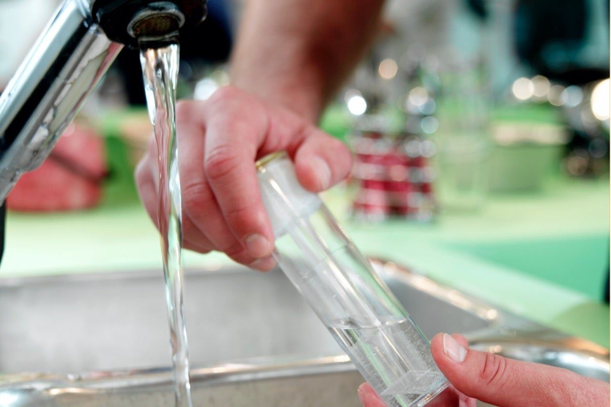A person is washing a bottle in a sink under a faucet.