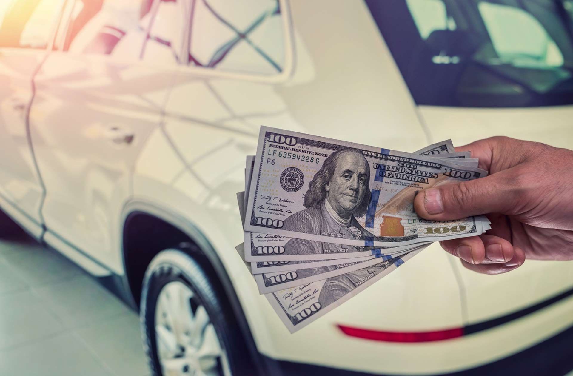 A person is holding a bunch of money in front of a car.