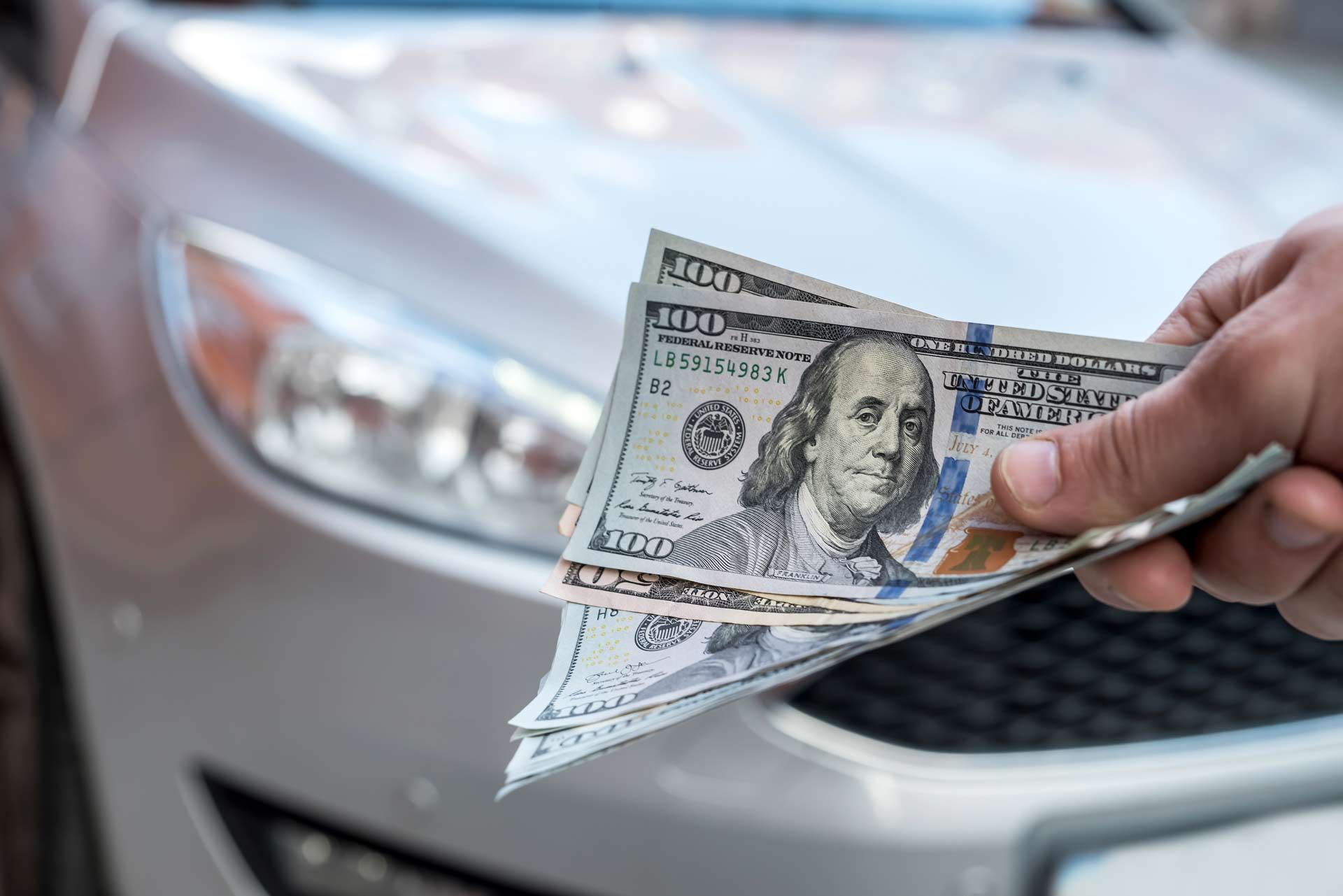 A person is holding a bunch of money in front of a car.
