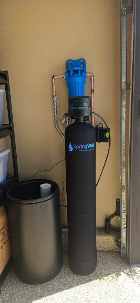 A water filter is sitting in a garage next to a trash can.