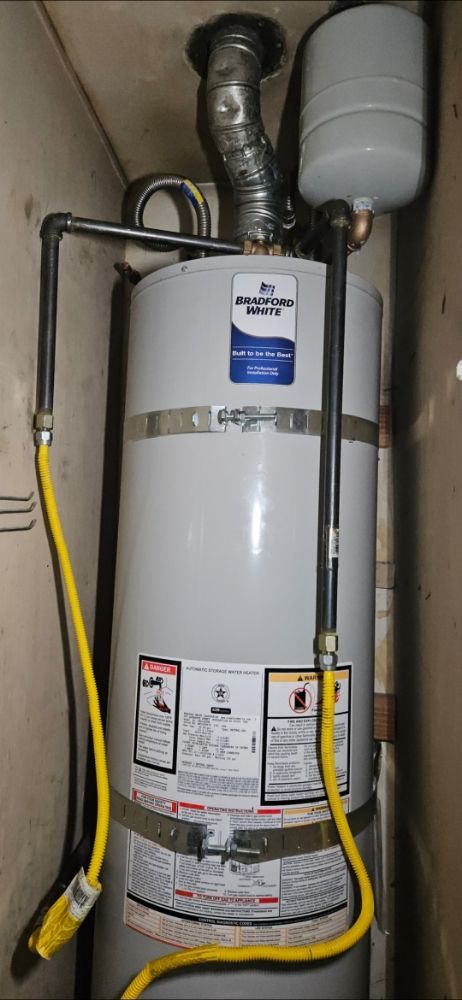A water heater is sitting in a corner of a room with a yellow hose attached to it.