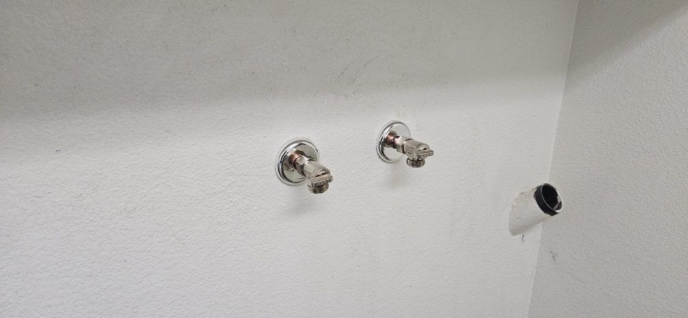 Two faucets are hanging on a white wall in a bathroom.