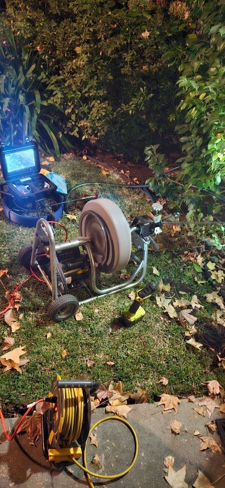 A drain cleaner is sitting on the grass next to a camera.