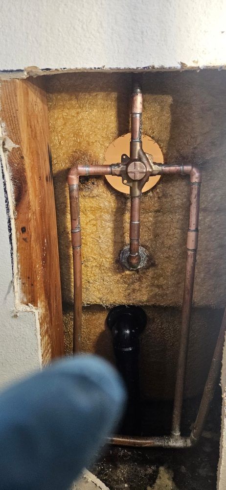 A person is holding a copper pipe in a hole in a wall.