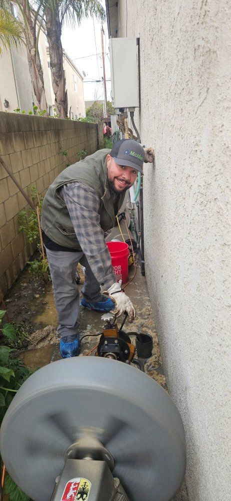 A man is using a drain cleaner to clean a drain on the side of a building.