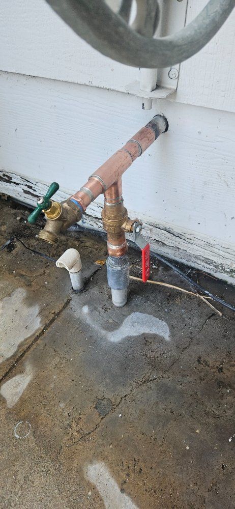 A close up of a copper pipe on the ground next to a wall.