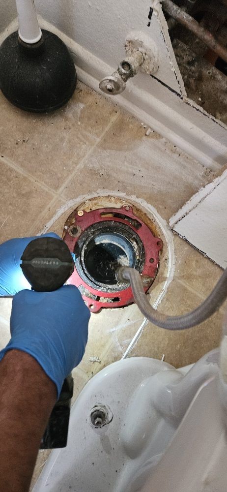 A person is using a plunger to remove a drain from a toilet.
