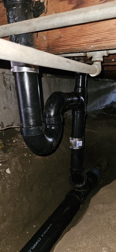 A black pipe is sitting under a wooden floor in a basement.