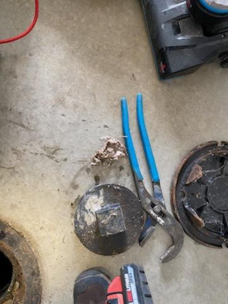 A pair of pliers is sitting on the floor next to a manhole cover.