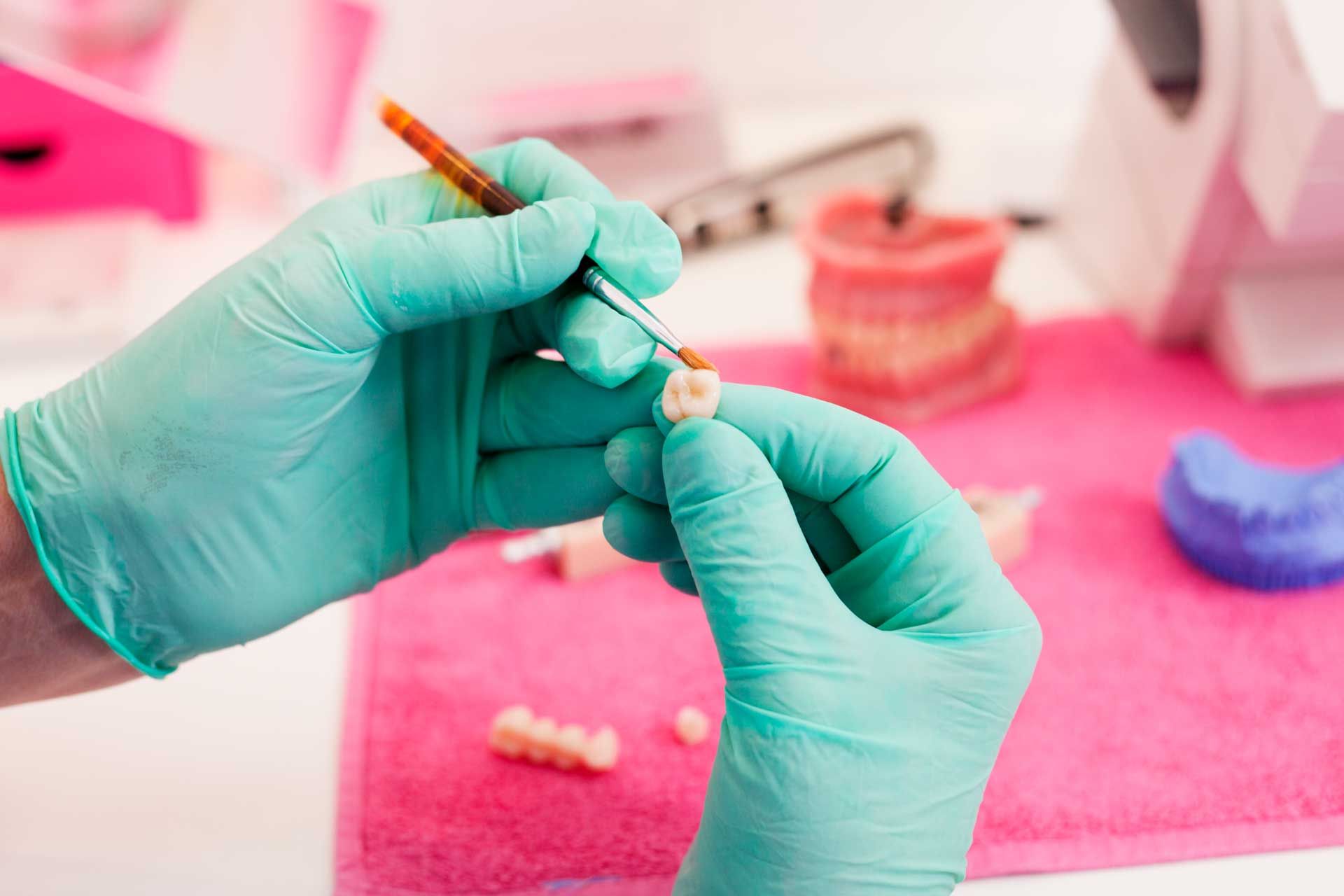Hands in green gloves holding dental crown, applying material with a small tool. Hands in green gloves holding dental crown, applying material with a small tool.