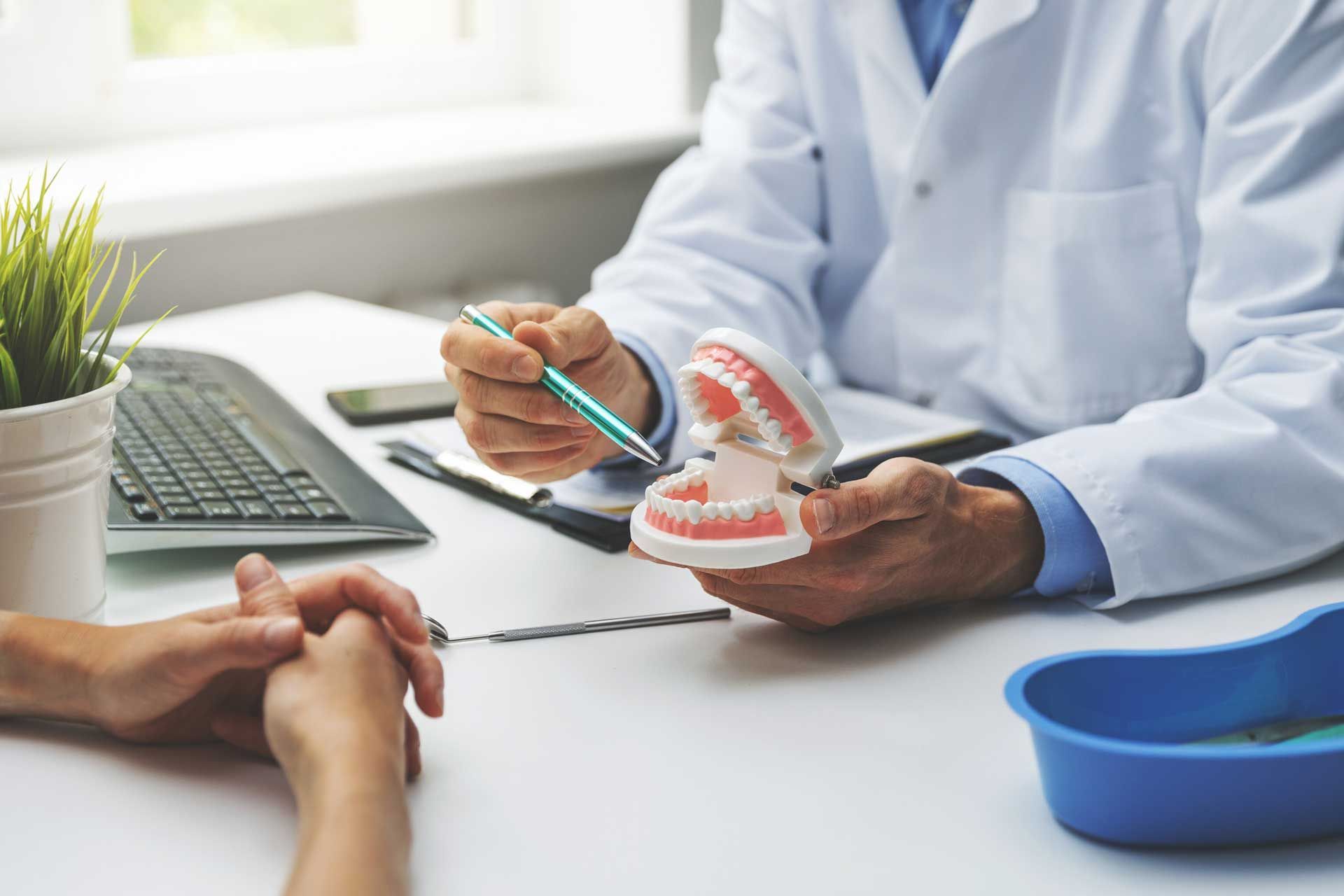 Dentist pointing at teeth model, explaining to a patient at a desk.