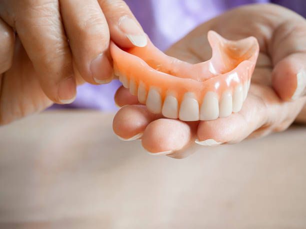 Person holding a set of upper dentures, showing pink gums and white teeth.