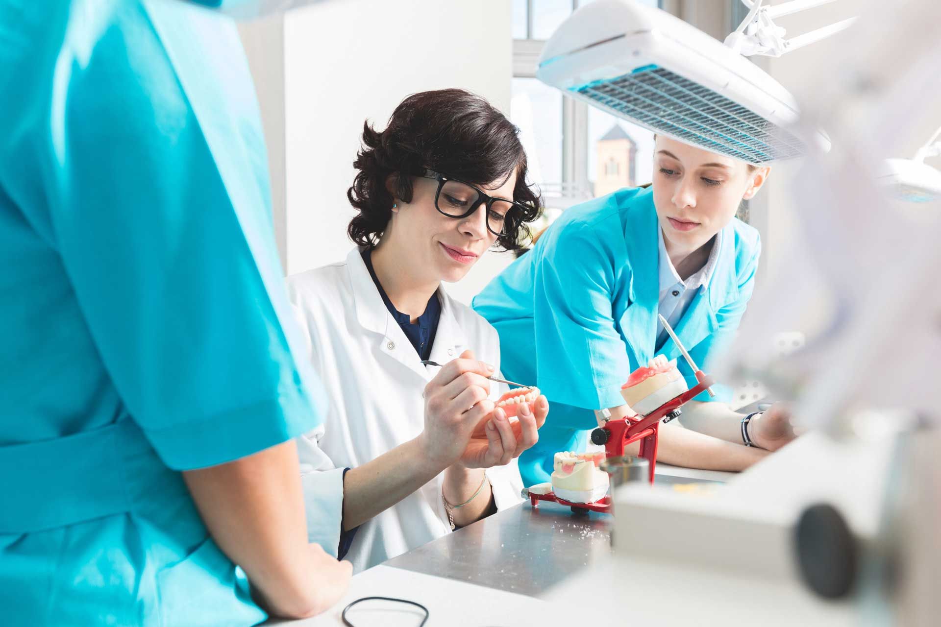 Three dental professionals examining models of teeth in a dental lab.