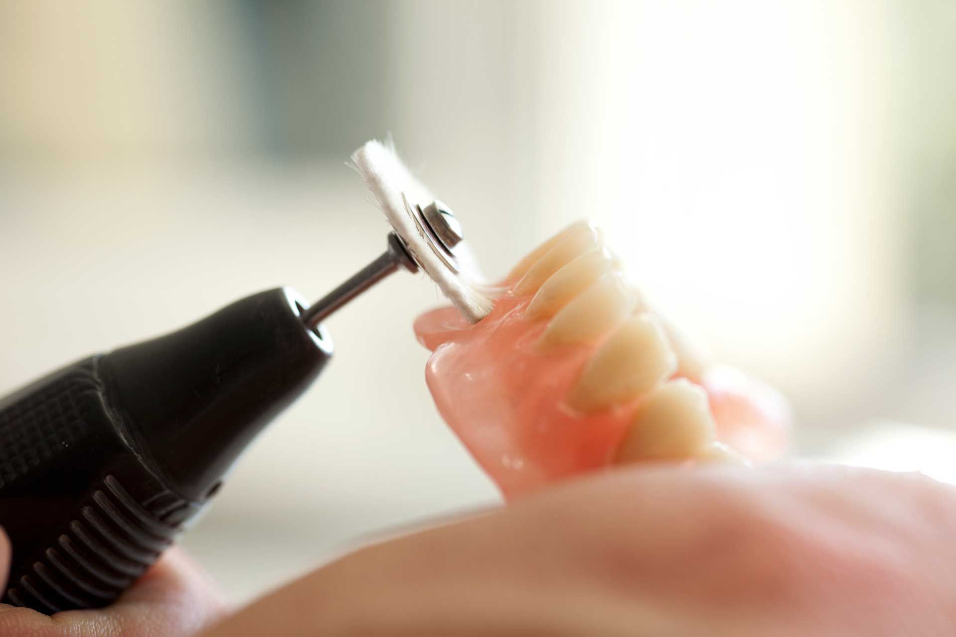 A dental technician using a rotary tool to adjust a set of dentures.