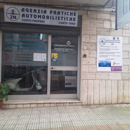 La vetrina di 2M, un'agenzia italiana di documentazione per veicoli, con un'insegna bianca e grigia e uno scooter visibile all'interno.