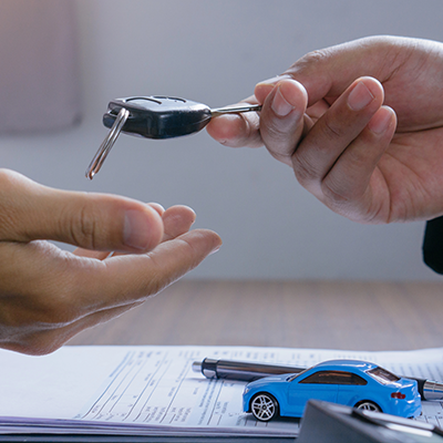 Una persona porge le chiavi dell'auto a un'altra persona, che si trova sopra una scrivania con dei documenti e una piccola macchinina blu.