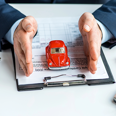 Un professionista in giacca e cravatta inquadra una macchinina rossa appoggiata su un documento assicurativo su una cartellina.