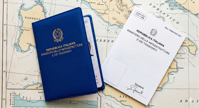 Un passaporto italiano blu e il relativo documento governativo bianco sono appoggiati su una vecchia cartina geografica.