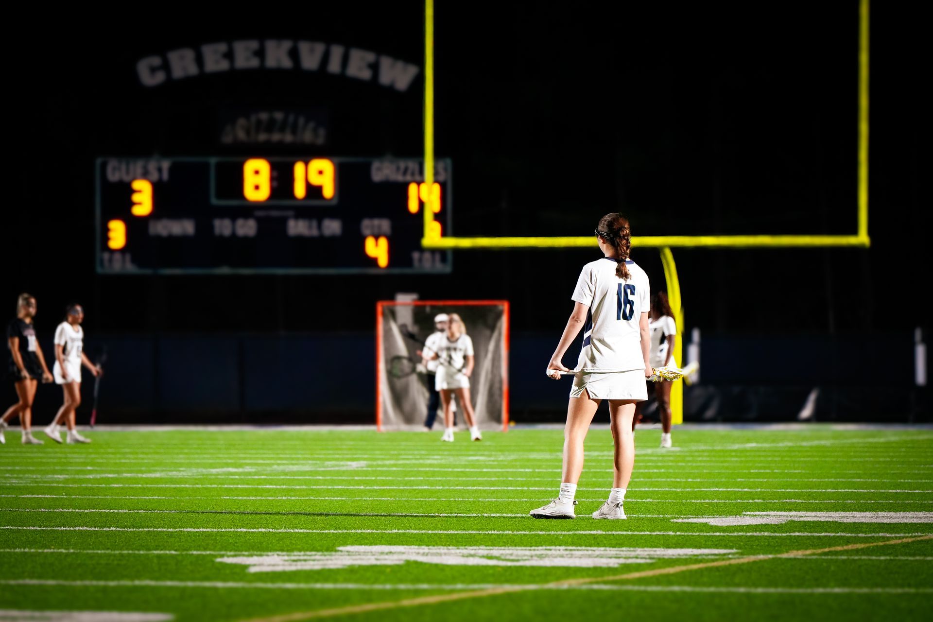 Girls high school lacrosse player on the field with scoreboard in the background