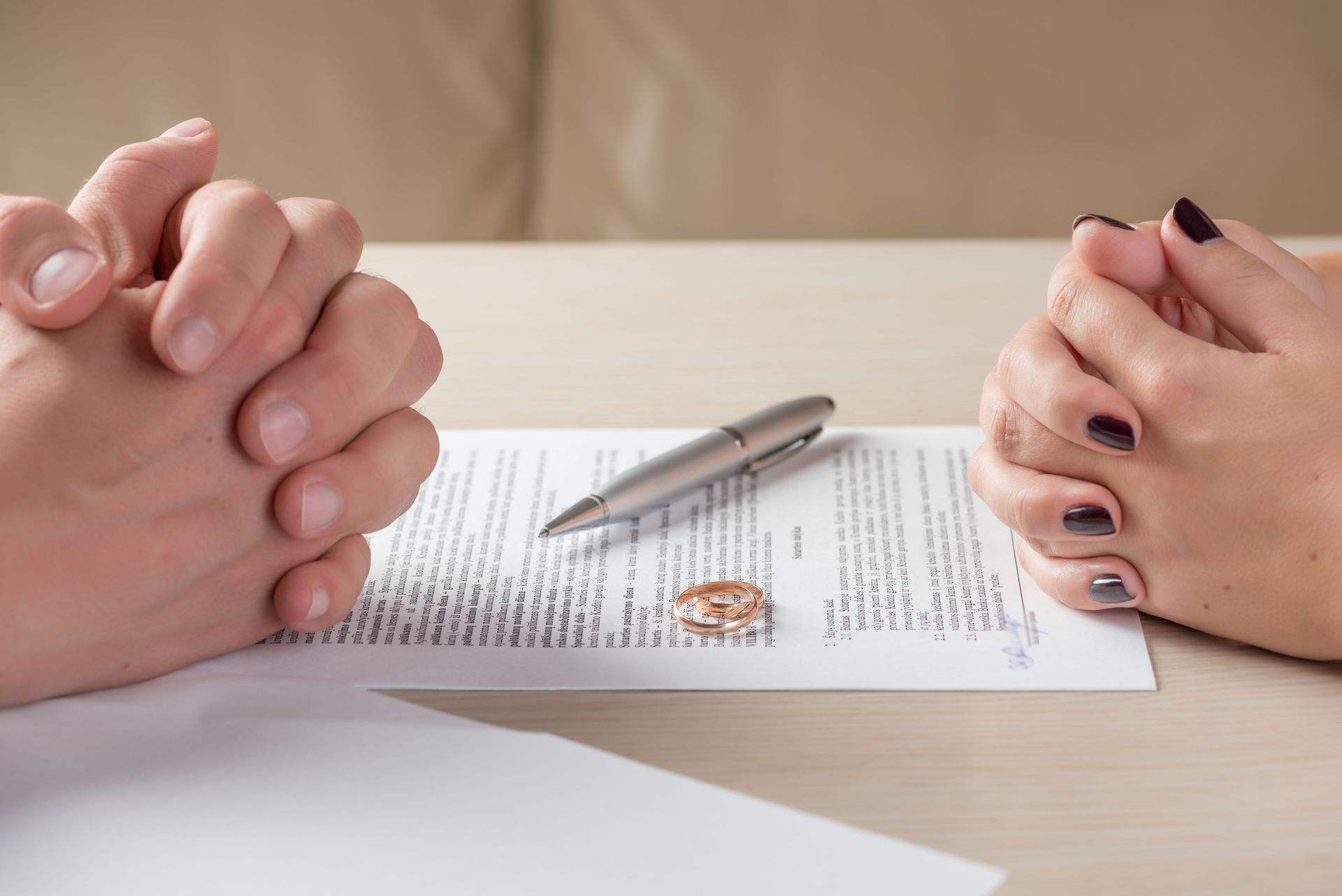 Two people’s hands clasped across a table beside a document and pen Two people’s hands clasped across a table beside a document and pen