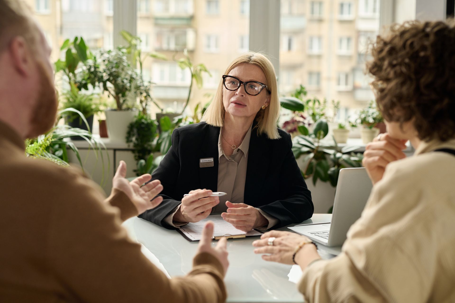 Attorney in a black blazer consulting with two clients at a desk with documents and a laptop nearby Attorney in a black blazer consulting with two clients at a desk with documents and a laptop nearby