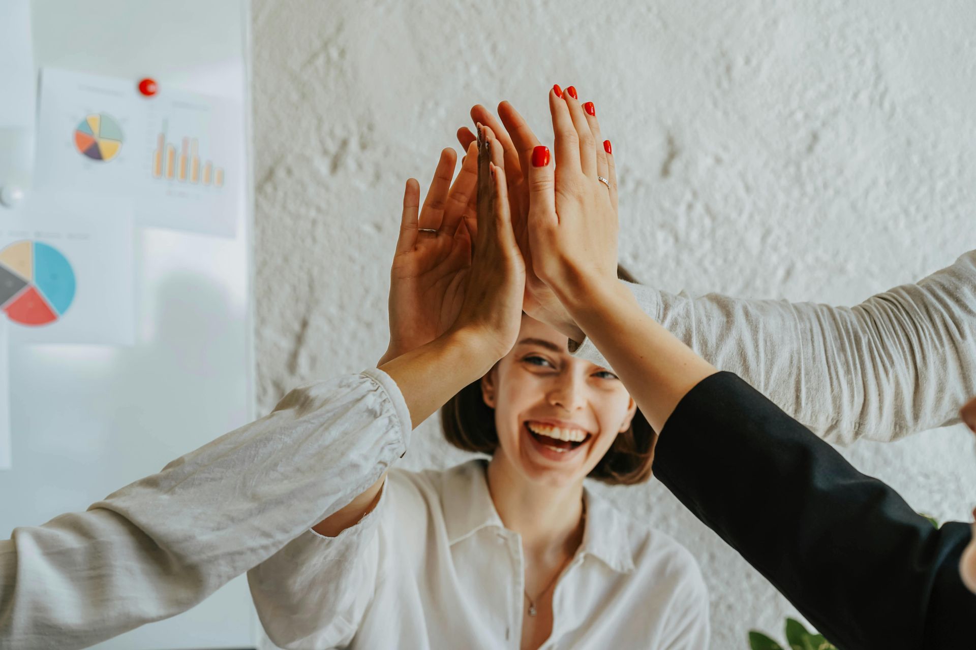 Woman standing in the background while three people off camera raise their hands for a high five