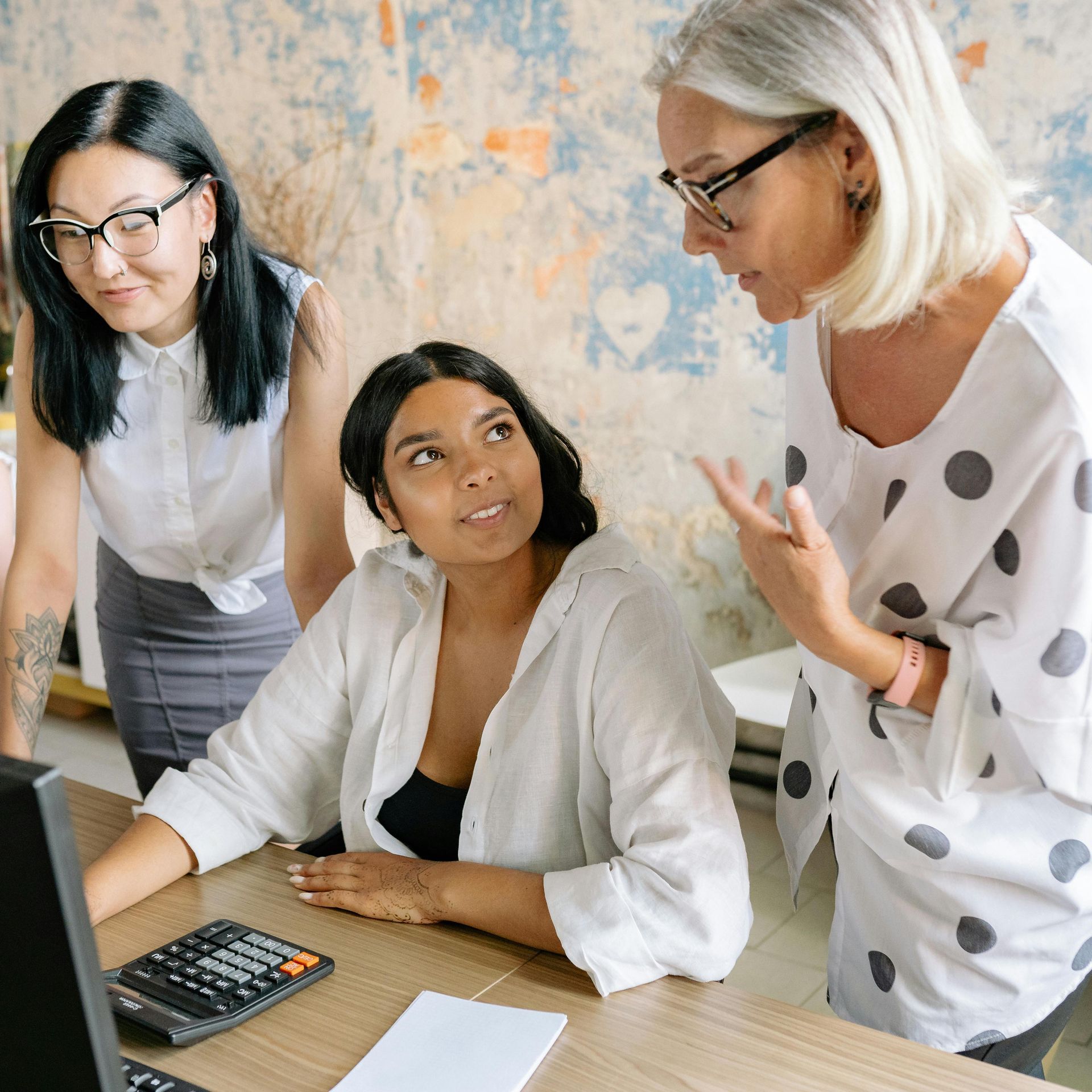 Three women standing and sitting together while brainstorming