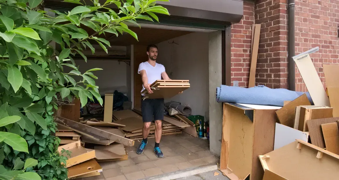 A man is carrying a box out of a garage filled with cardboard boxes.