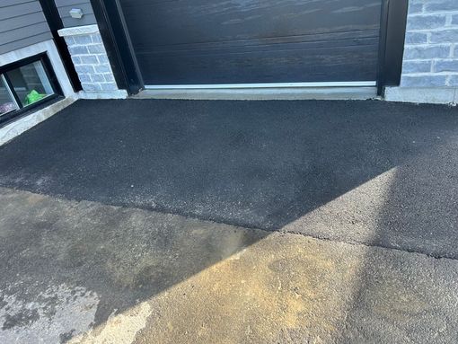 Une plaque d'asphalte sombre et fraîchement pavée contrastait avec le mur de la maison et la porte du garage en briques gris clair.