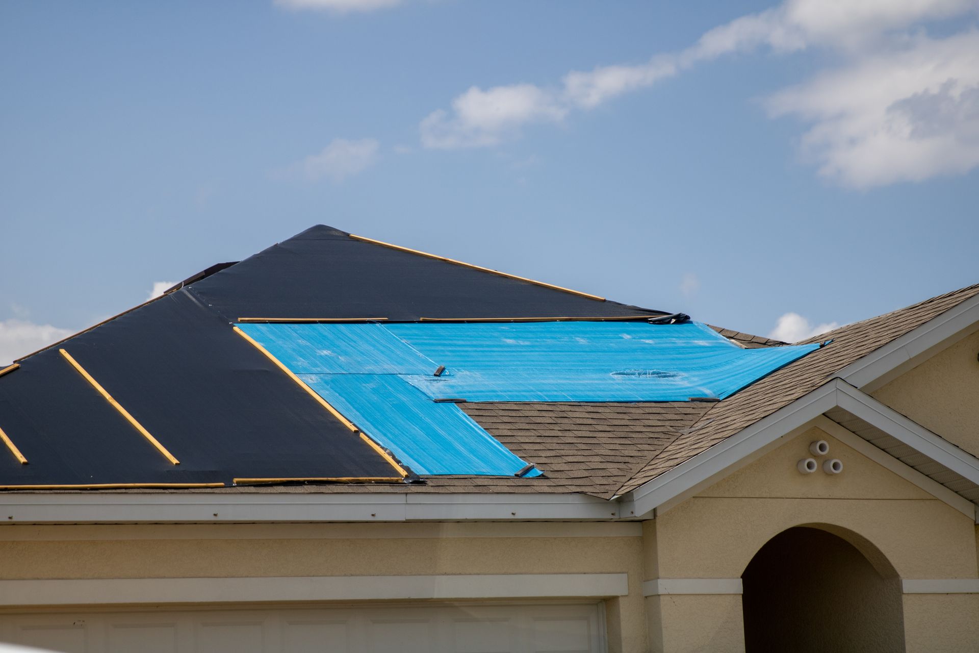 The roof of a house is being covered with a blue tarp.