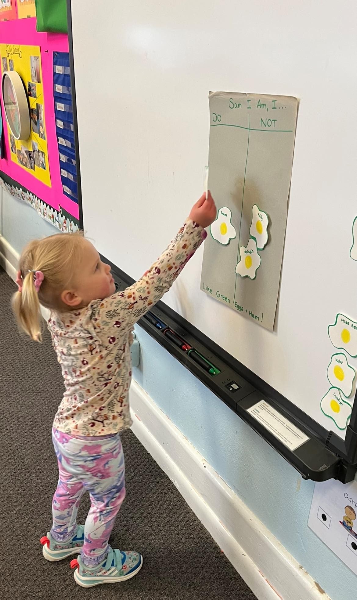 A little girl is standing in front of a whiteboard in a classroom.