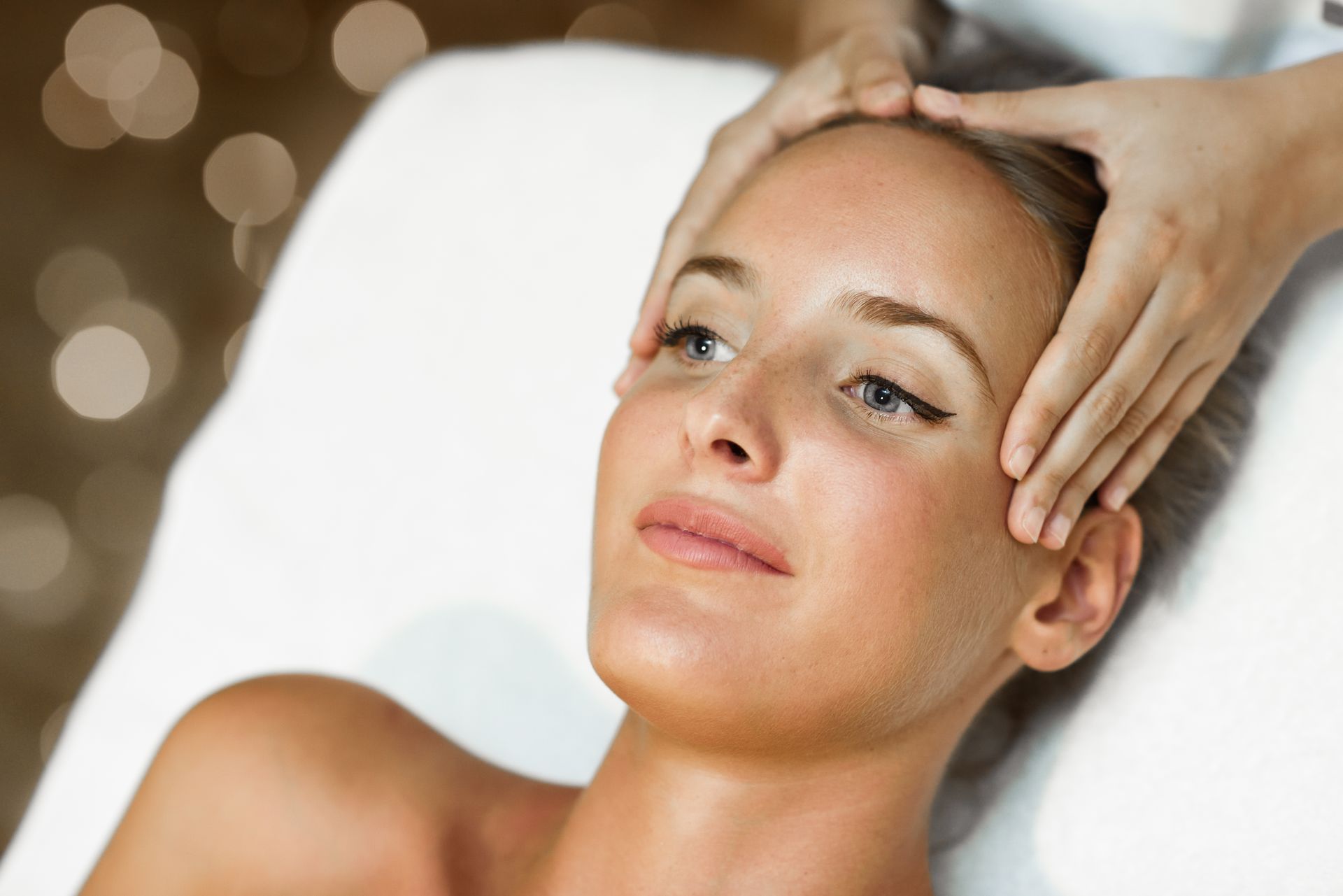 Woman receiving a face massage in a spa, hands on forehead, relaxed expression.