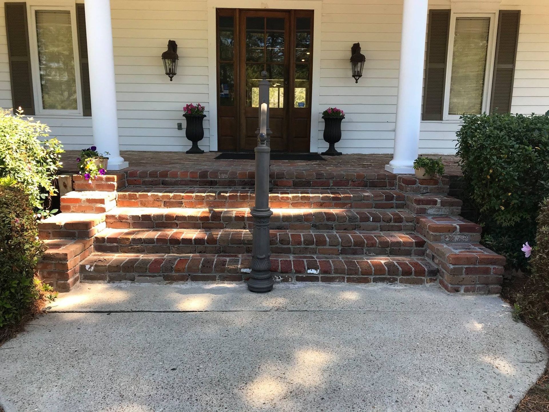 Brick steps lead to a white porch with columns and a brown door. Black lanterns flank the door.