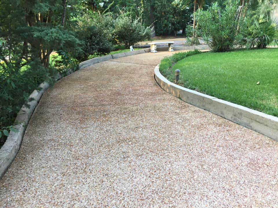 Curving gravel path with concrete borders next to green lawn and bushes.